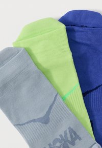 Τρία ζευγάρια διπλωμένων κάλτσων αστραγάλου σε γκρι, λαχανί και μπλε, τοποθετημένα δίπλα το ένα στο άλλο σε λευκό φόντο.