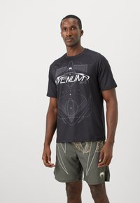 T-shirt noir à manches courtes avec un design graphique blanc sur le devant, associé à un short vert avec un motif de feuilles et des détails blancs.