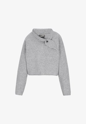 Lyhyt harmaa neule pehmeästä kankaasta, jossa on huppukaulus ja sivusolki. Kauluksessa on nappikoriste.