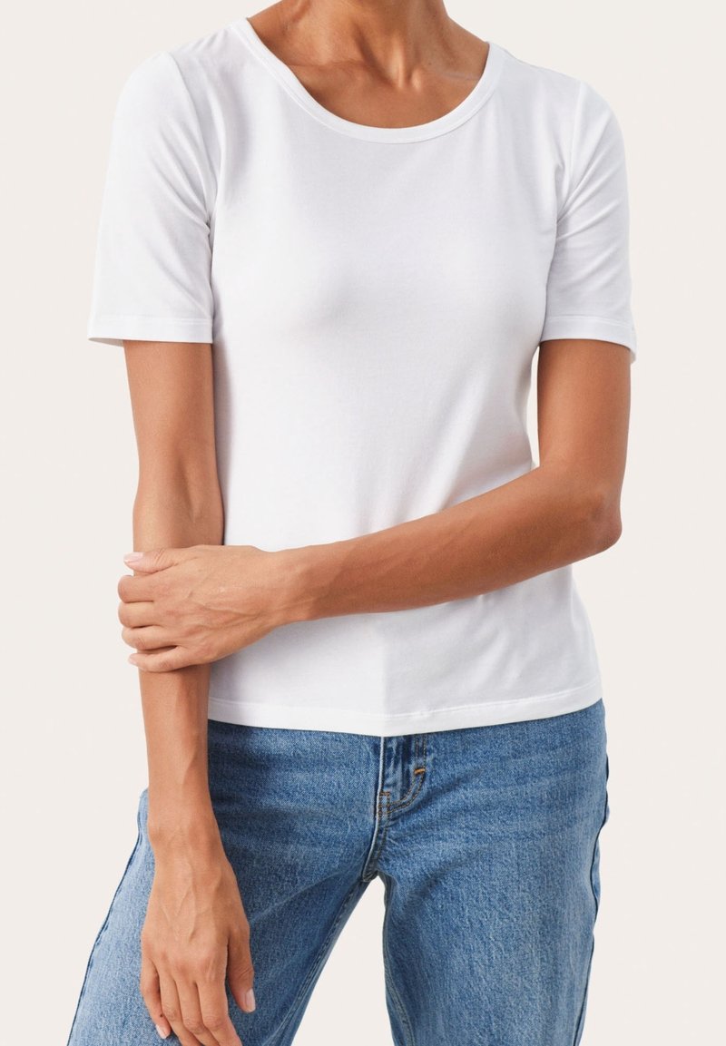 T-shirt blanc à manches courtes en coton doux. Il présente un col rond et une silhouette ajustée. Porté avec un jean en denim bleu décontracté.