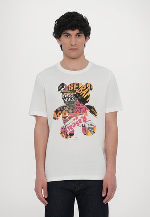 T-shirt de algodão branco com um design em forma de urso preenchido com gráficos coloridos e padrões e texto na parte da frente. Mangas curtas, gola redonda.