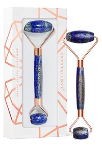 Niebieski kamienny roller do twarzy z wypolerowanymi końcówkami z lapis lazuli, złotymi metalowymi akcentami i charakterystycznym geometrycznym opakowaniem.