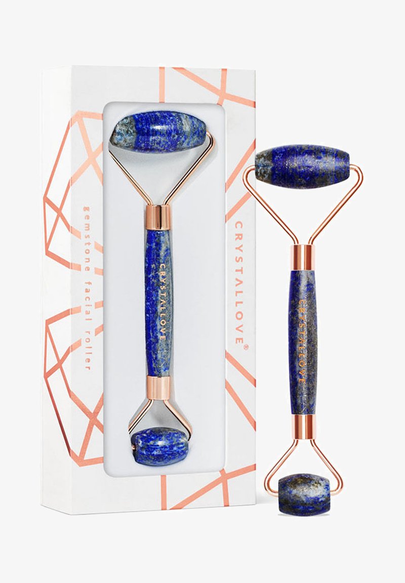 Niebieski kamienny roller do twarzy z wypolerowanymi końcówkami z lapis lazuli, złotymi metalowymi akcentami i charakterystycznym geometrycznym opakowaniem.