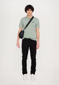 Polo shirt in light green with short sleeves and embroidered logo, paired with black jeans and white sneakers. Small black crossbody bag.