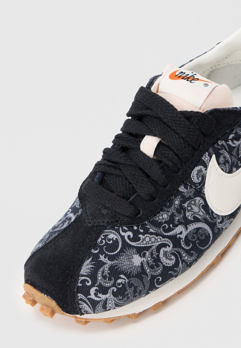 Sneaker nera con tomaia in tessuto caratterizzata da un elegante motivo grigio, logo Nike bianco, lacci neri e suola in gomma marrone con tacca.