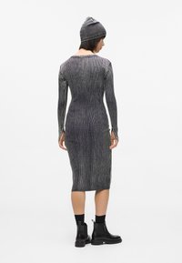 Vestido ajustado a la altura de la rodilla, hecho de tela de canalé de color gris oscuro. Mangas largas, cuello redondo, con aberturas laterales. Combinado con un gorro gris a juego.