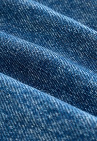 Tissu en denim dans différentes teintes de bleu, mettant en valeur un tissage texturé avec des fils clairs et foncés contrastés en vagues horizontales.