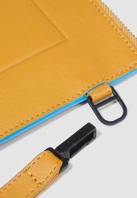 Borsa in pelle gialla con interno blu, dotata di accessori e cuciture nere. Include una tracolla con un gancio nero alla fine.