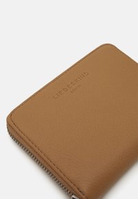 Braune Lederbörse mit strukturiertem Finish, ausgestattet mit einem Reißverschlussverschluss und geprägtem Markennamen. Quadratische Form mit abgerundeten Kanten.