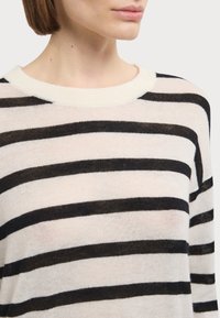 Pull en maille avec un col rond crème, présentant des rayures horizontales noires sur un tissu doux et léger. Design sans coutures.