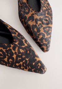 Chaussures pointues imprimé léopard en fourrure texturée, présentant un mélange de motifs marron doré et noir, avec une doublure intérieure noire.