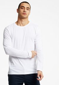 Langærmet hvid T-shirt lavet af letvægtsbomuld, med rund halsudskæring og tætsiddende design. Glat tekstur, uden mønstre eller accenter.