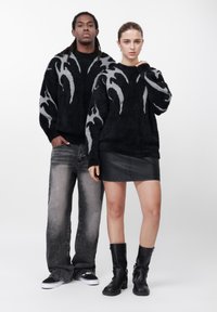 Črni puhasti puloverji z sivimi vzorci v obliki plamenov, kombinirani z raztrganimi sivimi kavbojkami in črno usnjeno krilo. Črni škornji s peto zaokrožujejo videz.