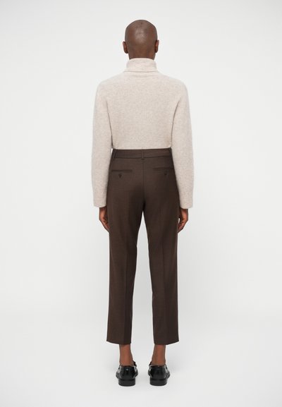 Μπεζ πλεκτό πουλόβερ με ψηλό λαιμό και σκούρες καφέ κομμένα παντελόνια. Τα παντελόνια διαθέτουν πίσω τσέπες και σχέδιο κωνικού ποδιού. Μαύρα παπούτσια ολοκληρούν το σύνολο.