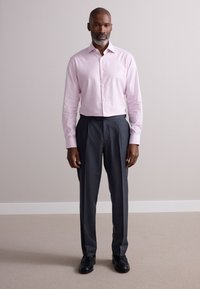 Heleroosa triibuline nööbitav särk, kohandatud istuvus, kombineeritud tumeda halli pükstega. Mustad nahast kingad, sile tekstuur ja teravad jooned.