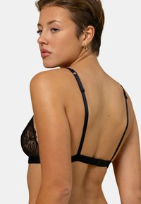 Bralette en dentelle noire avec un motif floral, fines bretelles ajustables et un fermoir croisé au dos. Texture douce.