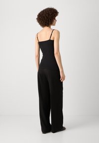 Black tank top with thin straps and a fitted design, paired with loose black wide-leg pants. The outfit has a smooth texture.