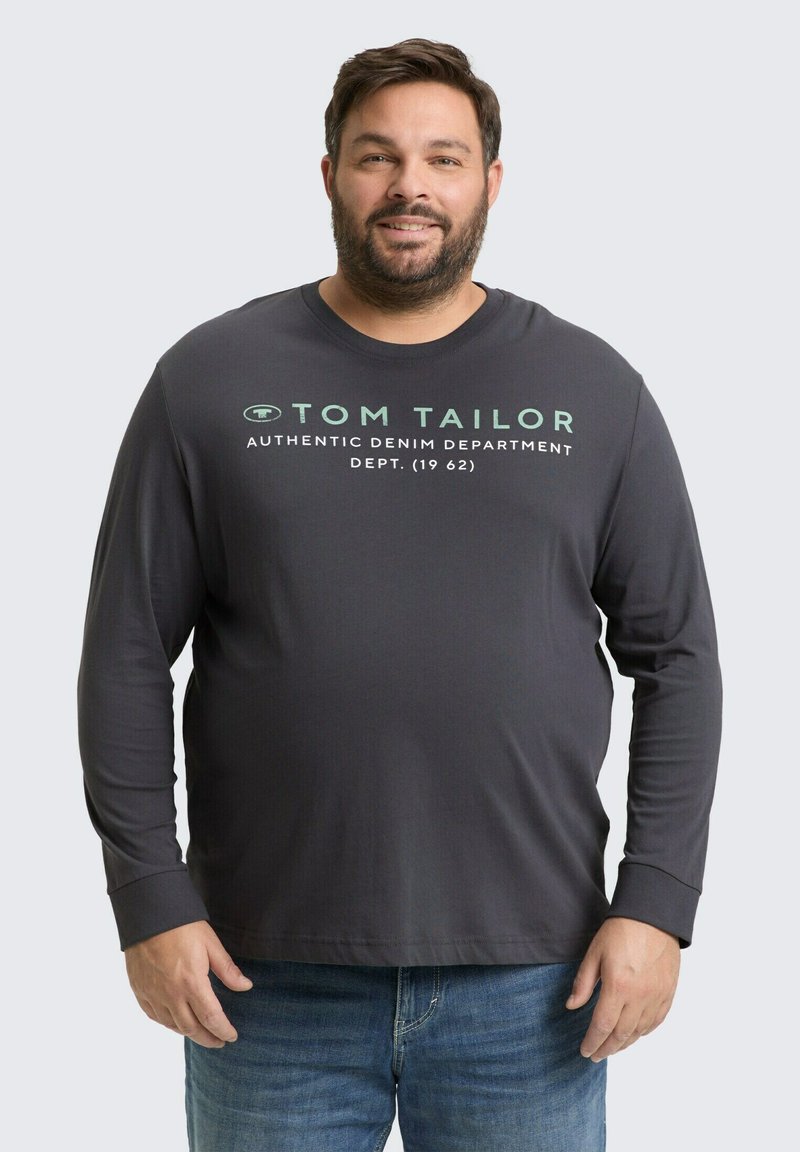 Donkergrijze langeklokken T-shirt met een ronde hals, voorzien van groene tekst die luidt "TOM TAILOR AUTHENTIC DENIM DEPARTMENT DEPT. (1962)."