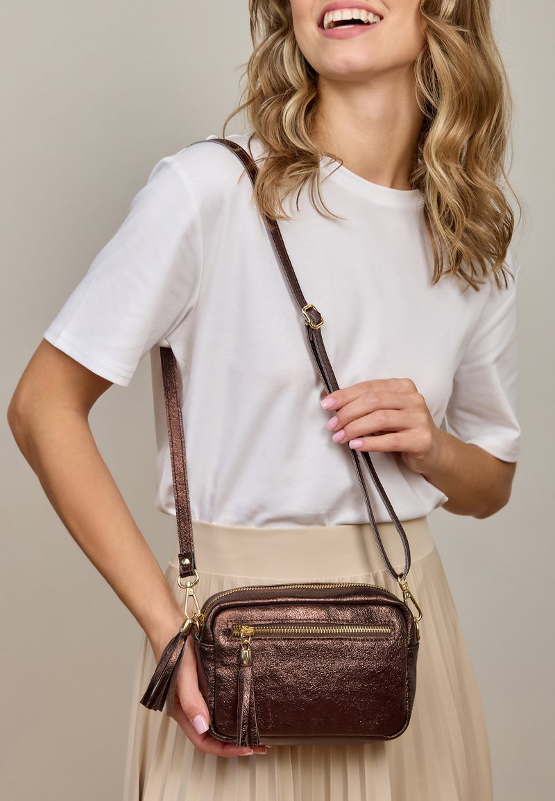 Smeđi metalik crossbody torba s dva zipovana odjeljka, zlatnim detaljima i naglaskom s resicama. Podesiva naramenica, pravokutnog oblika.