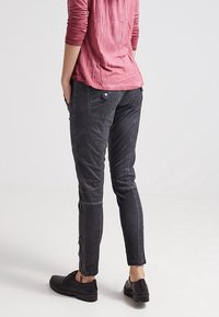 Zwarte slim-fit broek met een gestructureerde afwerking, voorzien van ritsen bij de enkels en een enkele knop op de achterzak.