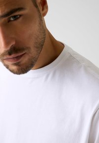 Weißes Baumwoll-T-Shirt mit rundem Ausschnitt, das eine weiche Textur und glatte Nähte aufweist. Nahaufnahme des Stoffes und des Kragenbereichs.