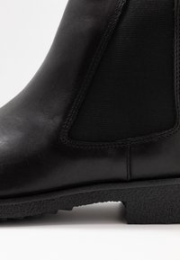 Botte Chelsea en cuir noir avec panneaux latéraux élastiques et semelle en caoutchouc texturé, présentant des lignes épurées et un minimum de détails.