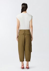 Bijela bluza s kapicama u kombinaciji s maslinasto zelenim cargo hlačama koje imaju elastičnu stražnju traku i bočne džepove. Crvene sandale upotpunjuju ovaj outfit.