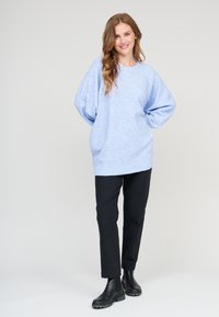 Helles blaues, übergroßes Sweatshirt mit rundem Ausschnitt und überschnittenen Schultern, kombiniert mit schwarzen, schmal geschnittenen Hosen und schwarzen Stiefeletten. Glatte Textur.