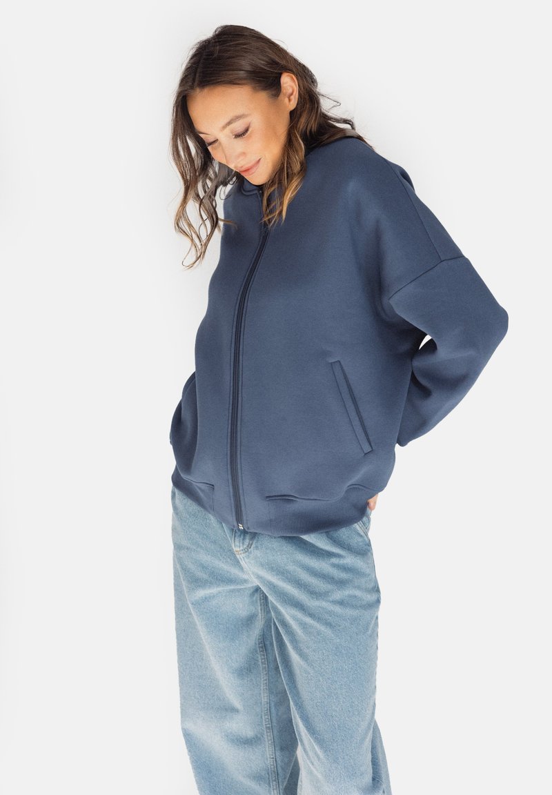 Granatowa bluza zapinana na zamek, wykonana z grubego materiału, o luźnym kroju, z dwoma bocznymi kieszeniami i opadającymi ramionami dla zapewnienia komfortowego dopasowania.