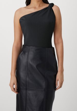 Kvinde iført en sort one-shoulder top med knudedetalje kombineret med et sort, højtaljet lædernederdel med synlige syninger.