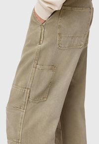 Beige cotton cargo pants with side and back pockets, featuring reinforced stitching and a textured finish. Relaxed fit design for comfort.