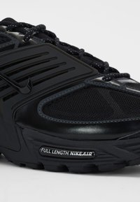 Gros plan d'une basket Nike noire avec tissu en mesh, superpositions synthétiques, lacets et étiquette "Full Length Nike Air" visible sur la semelle.