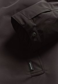 Ciemnobrązowy rękaw kurtki o gładkiej, błyszczącej fakturze. Zapięcie na zatrzask oraz czarna metka z napisem "Martinique" przyszyta do materiału.