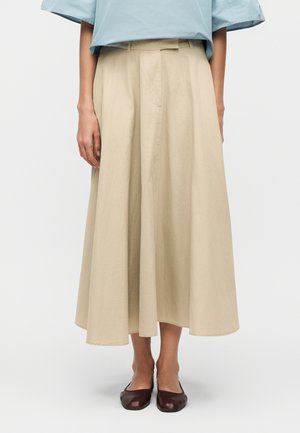 Woman wearing a beige wide-leg midi skirt with a high waist, paired with dark brown flat shoes and a light blue top.