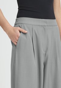 Grå bukser med brede ben og sidelommer samt en flad front. Har en glat tekstur og en elastisk talje for ekstra komfort.