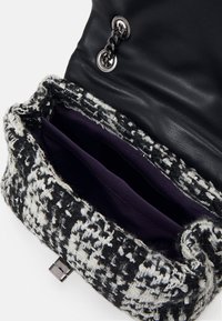 Borsa a tracolla nera in pelle con pattina lavorata a motivo houndstooth. L'interno presenta due scomparti con rivestimento di un profondo colore viola. Dettagli in hardware argentato.
