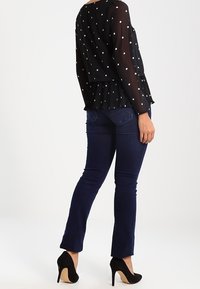 Blusa nera a pois, semi-trasparente, con orlo a peplo; abbinata a jeans blu scuro e scarpe con tacco nere.