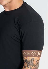 Černé tričko s krátkým rukávem s hnědým pruhem kolem rukávu s logy; hladká tkanina, přiléhavý střih a kulatý výstřih.