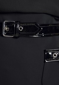 Ceinture noire brillante avec boucle et œillets argentés sur fond en tissu noir.