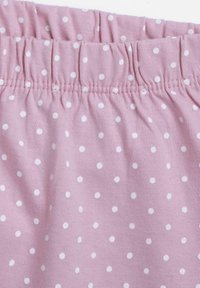 Ljust rosa tyg med vita prickar; har en elastisk midja och mjuk, slät textur. Närbilden framhäver mönstret.