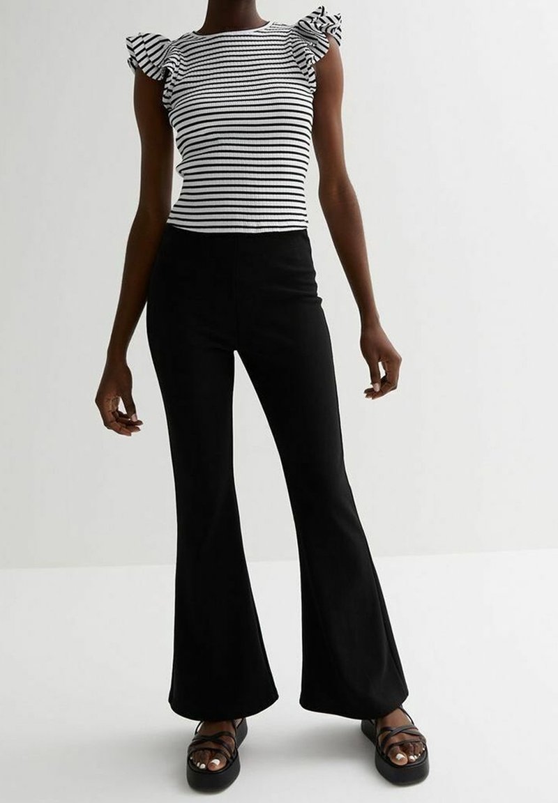 Pruhovaný černo-bílý žebrovaný top s volánovými rukávy, v kombinaci s vysokým pasem černými rozšířenými kalhotami a masivními černými sandály.