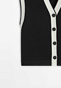 Svart ärmlös cardigan med vit kant, fem svarta knappar, ribbad textur och V-halsdesign.