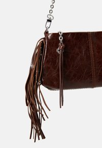 Bruine leren tas met franjes, rechthoekige vorm, glanzende afwerking en een zilveren kettingriem. Heeft een subtiele gekreukelde textuur.