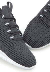 Grijze sportieve sneakers van structuurbreisels, met witte accenten, een vetersluiting en een stevige witte rubberen zool.