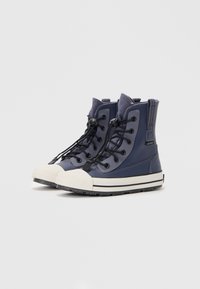 Zapatillas náuticas impermeables de caña media en color navy, con ojales negros, cordones planos, una puntera de goma blanca y una suela texturizada negra.