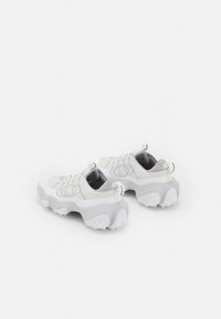 Weiße Mesh-Sneaker mit grauen Gummielementen, runder Form, strukturierten Sohlen und elastischen Schnürsenkeln. Mit einem runden Logo an den Seiten.