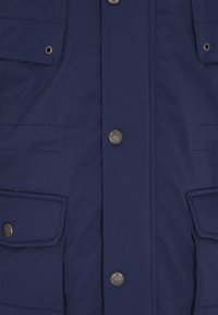 Navyblå jakke lavet af blødt stof med knaplukning fortil, to brystlommer og sølvfarvede hardware-detaljer. Glat tekstur med synlig syning.