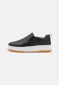 Shoe slip-on preto com parte superior em couro liso, entressola branca e sola de borracha marrom. Apresenta elástico lateral para fácil colocação.