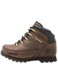 Brązowy skórzany but wędrówkowy z czarnymi akcentami, złotymi oczkami, wyściełanym kołnierzem, teksturowaną gumową podeszwą oraz logo Timberland po boku.