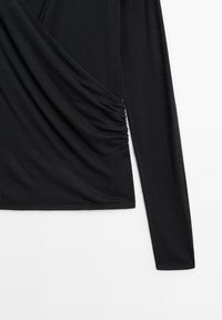 Czarna bluzka z długim rękawem o fasonie drapowanym, z marszczeniami po bokach i miękkim, elastycznym materiałem.